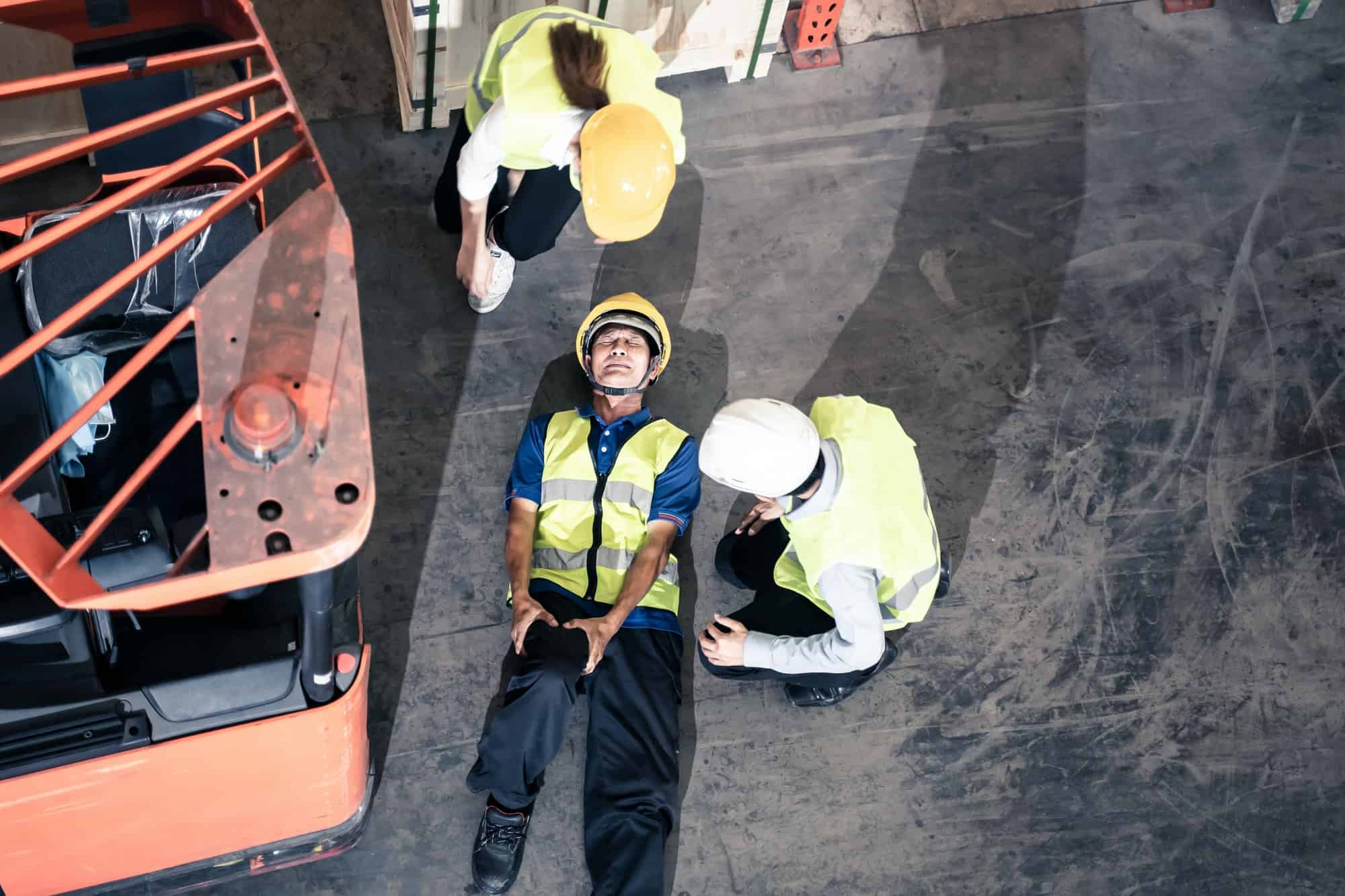 Asian man worker had accident broken his leg lying near forklift truck on floor in warehouse.